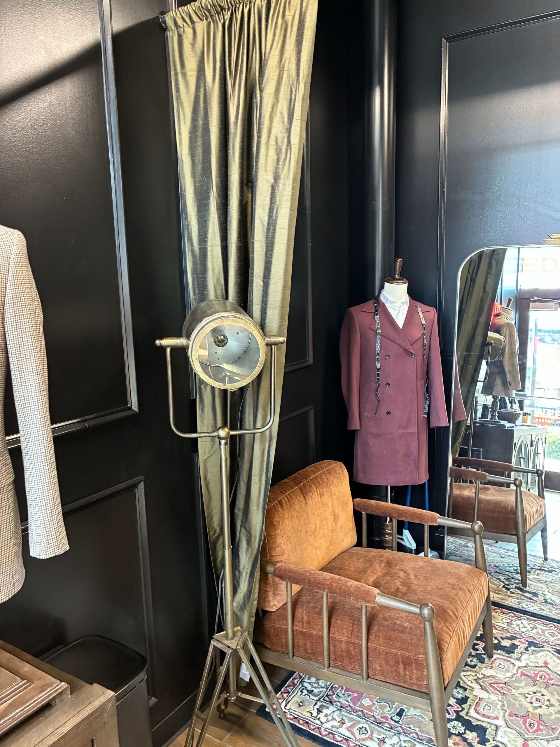 Vintage clothing store display with a floor lamp, chair, and mannequin in front of a mirror.