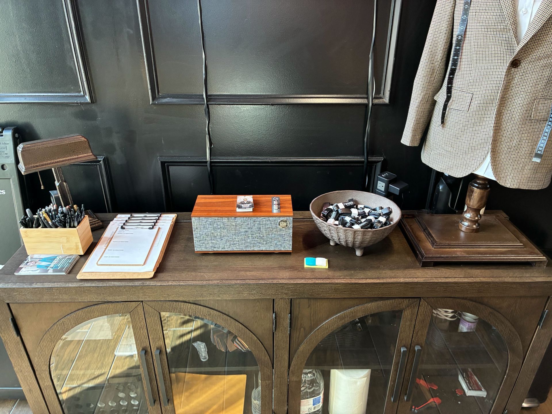 A wooden cabinet displays pens, a clipboard, a box, a bowl of items, and a jacket on a mannequin.