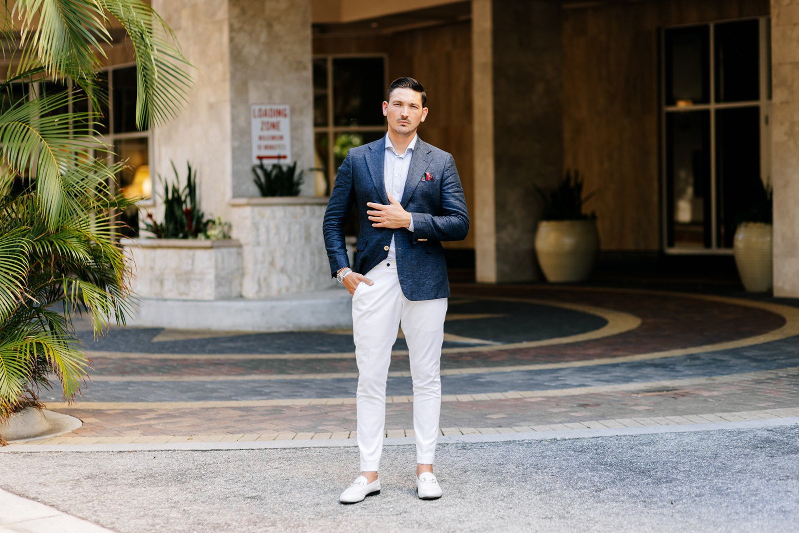 A man in a suit and white pants is standing in front of a building.