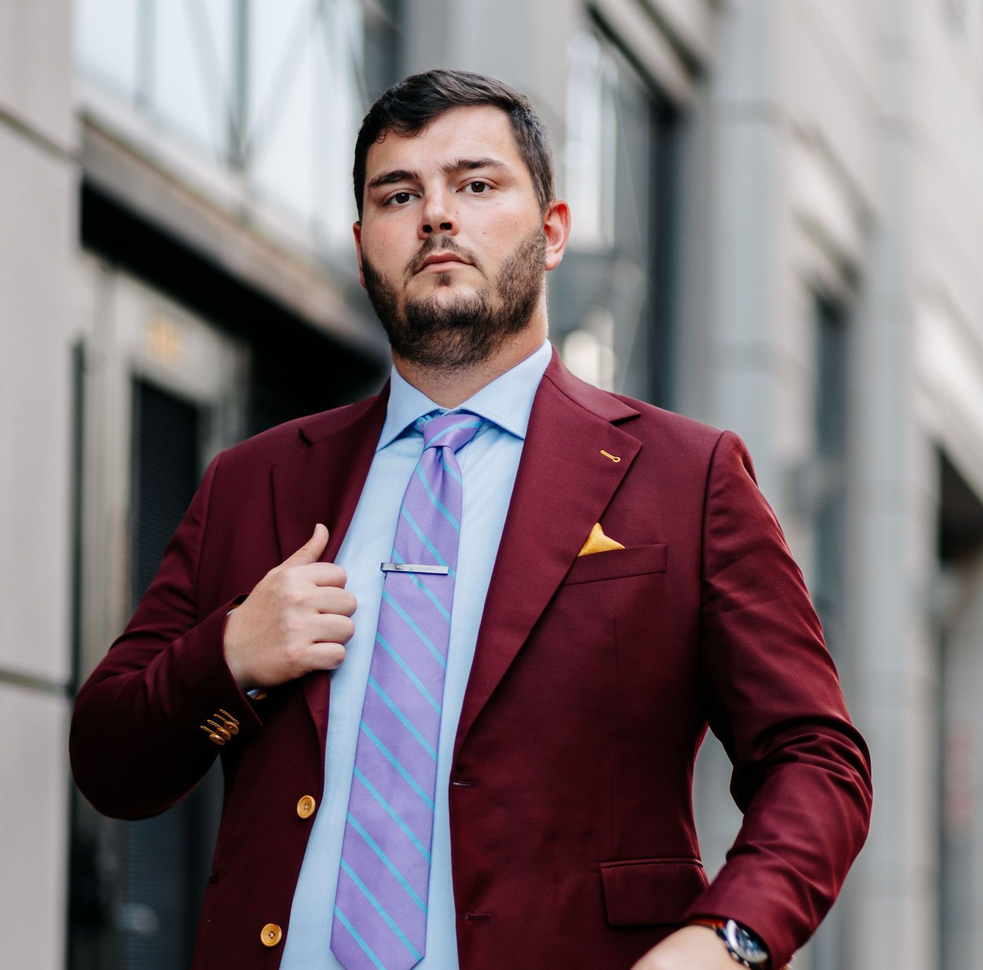 A man in a maroon suit and tie is standing in front of a building.
