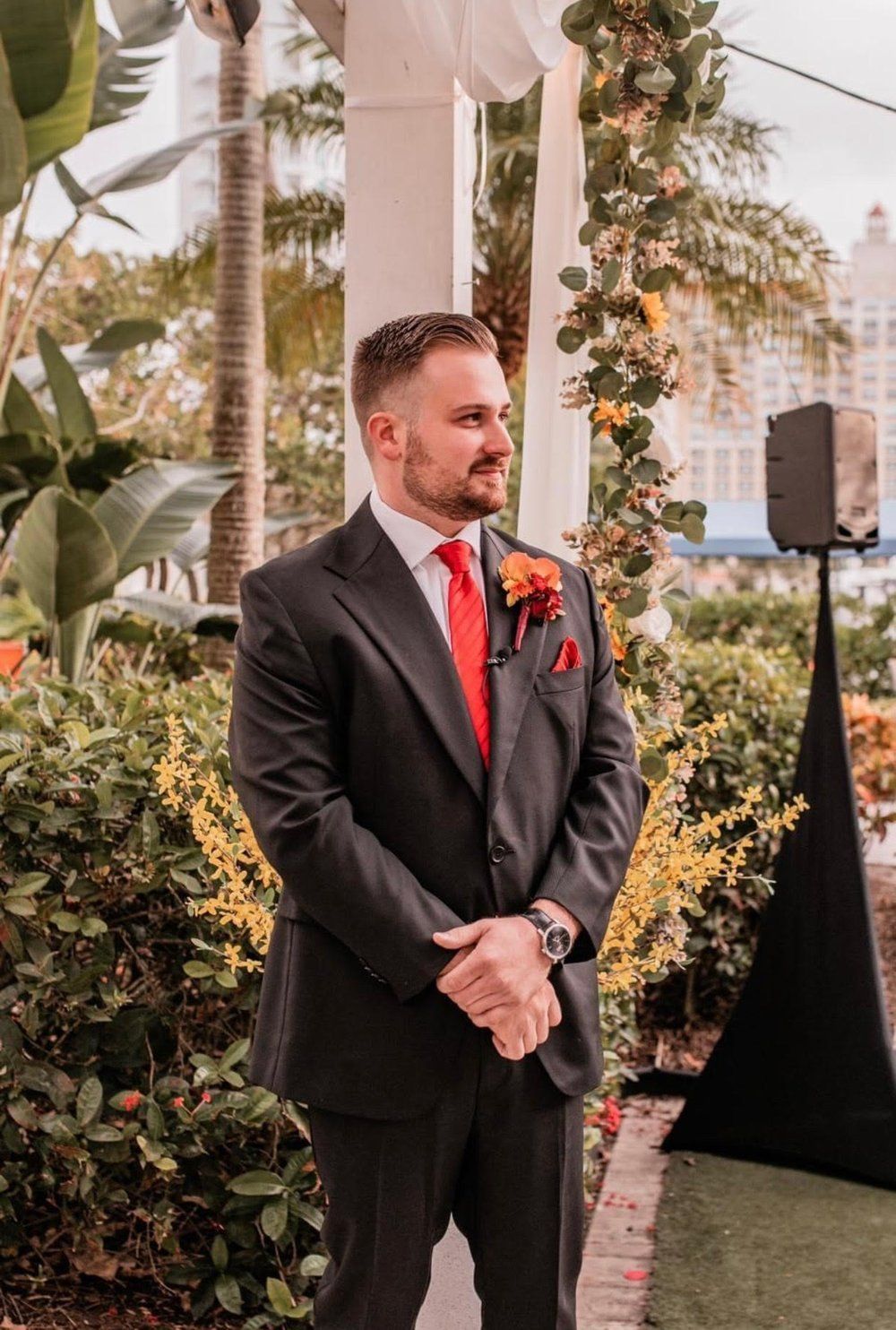 A man in a suit and red tie is standing in front of a white archway.