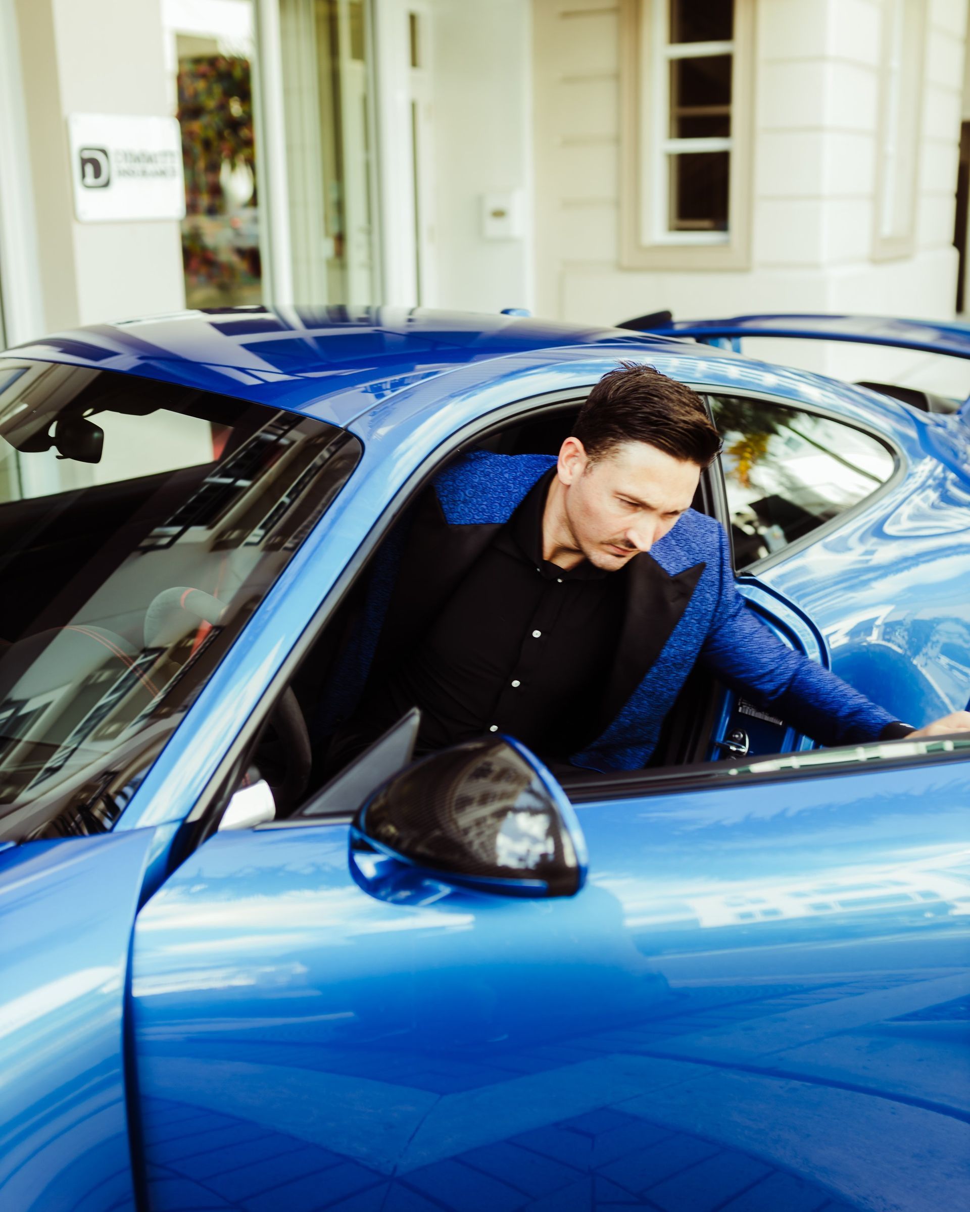 A man in a suit is getting out of a blue sports car