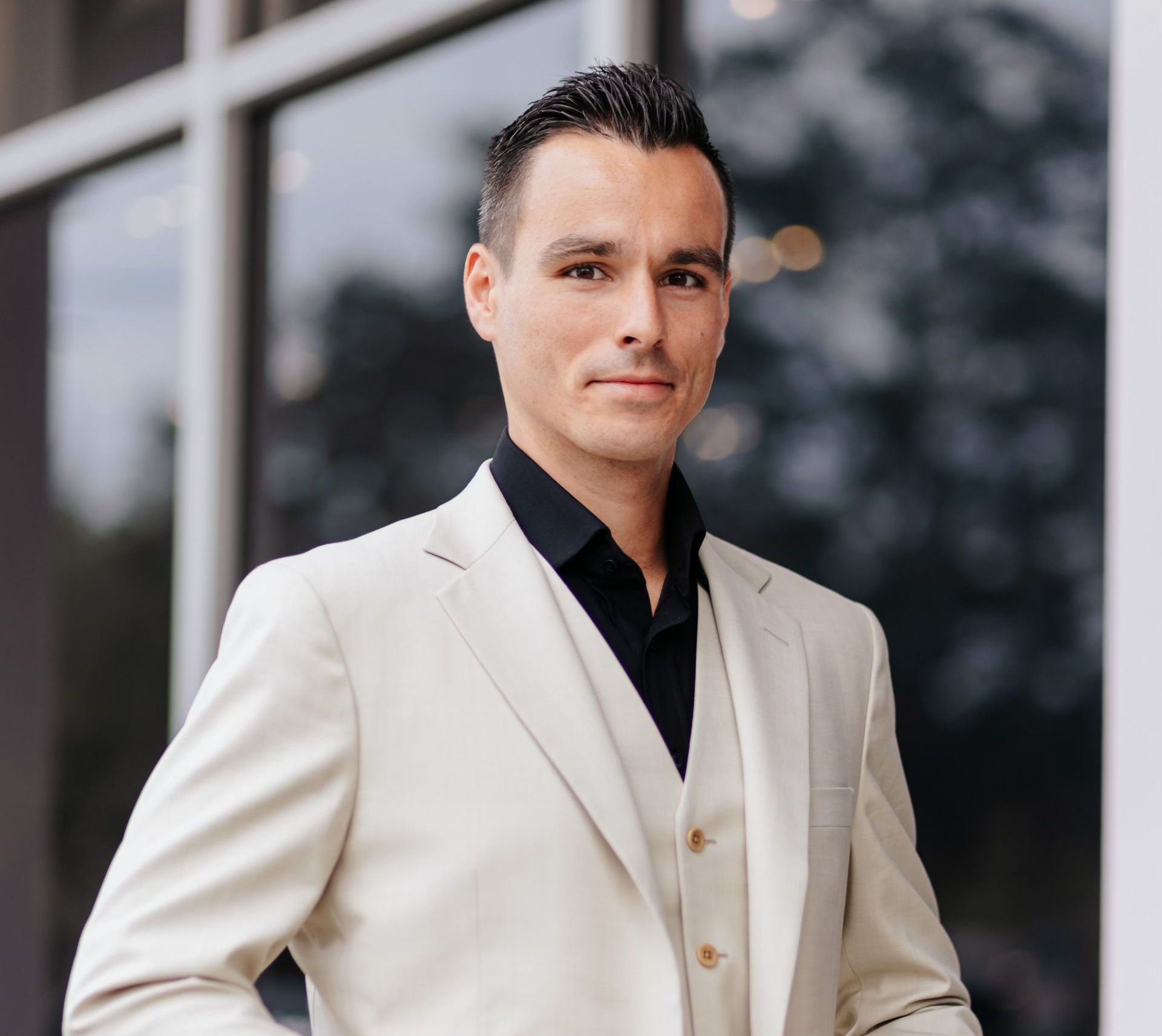 A man in a white suit and black shirt is standing in front of a building.