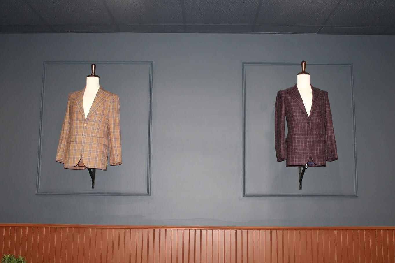 Two jackets displayed on mannequins against a blue wall. One is brown, the other is purple.