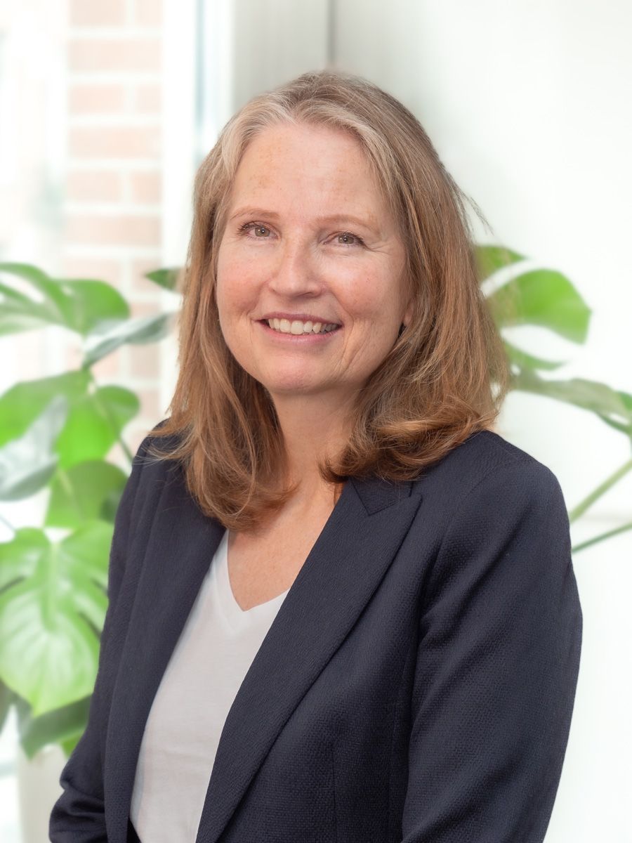 Een vrouw in een pak en een wit overhemd lacht naar de camera.