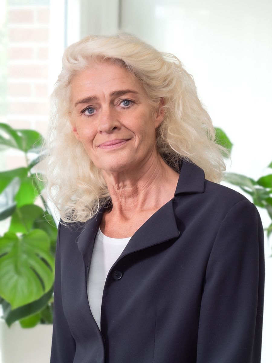 Een vrouw met blond haar draagt een blauw jasje en lacht.