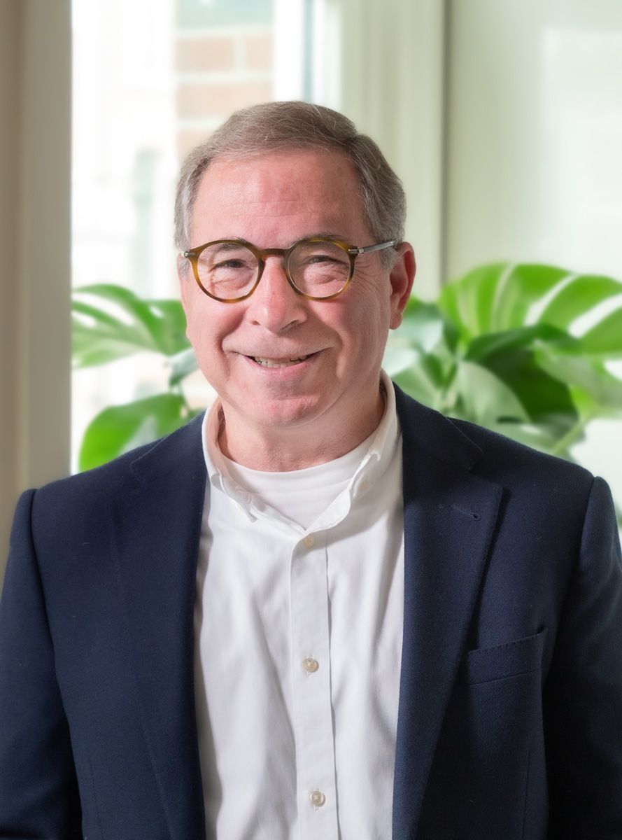 Een man in pak en bril lacht naar de camera.