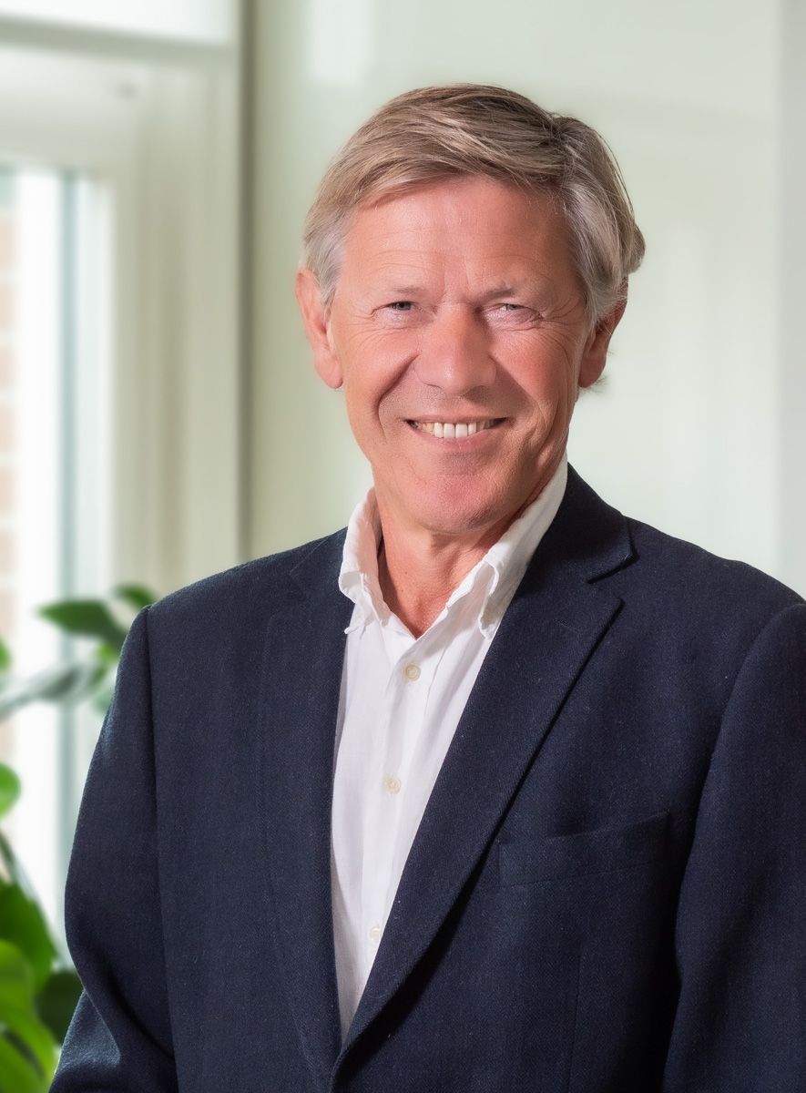 Een man in een pak en een wit overhemd lacht naar de camera