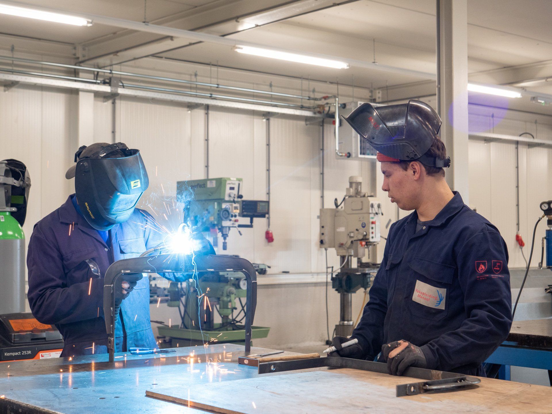 Twee mannen lassen een stuk metaal in een fabriek.