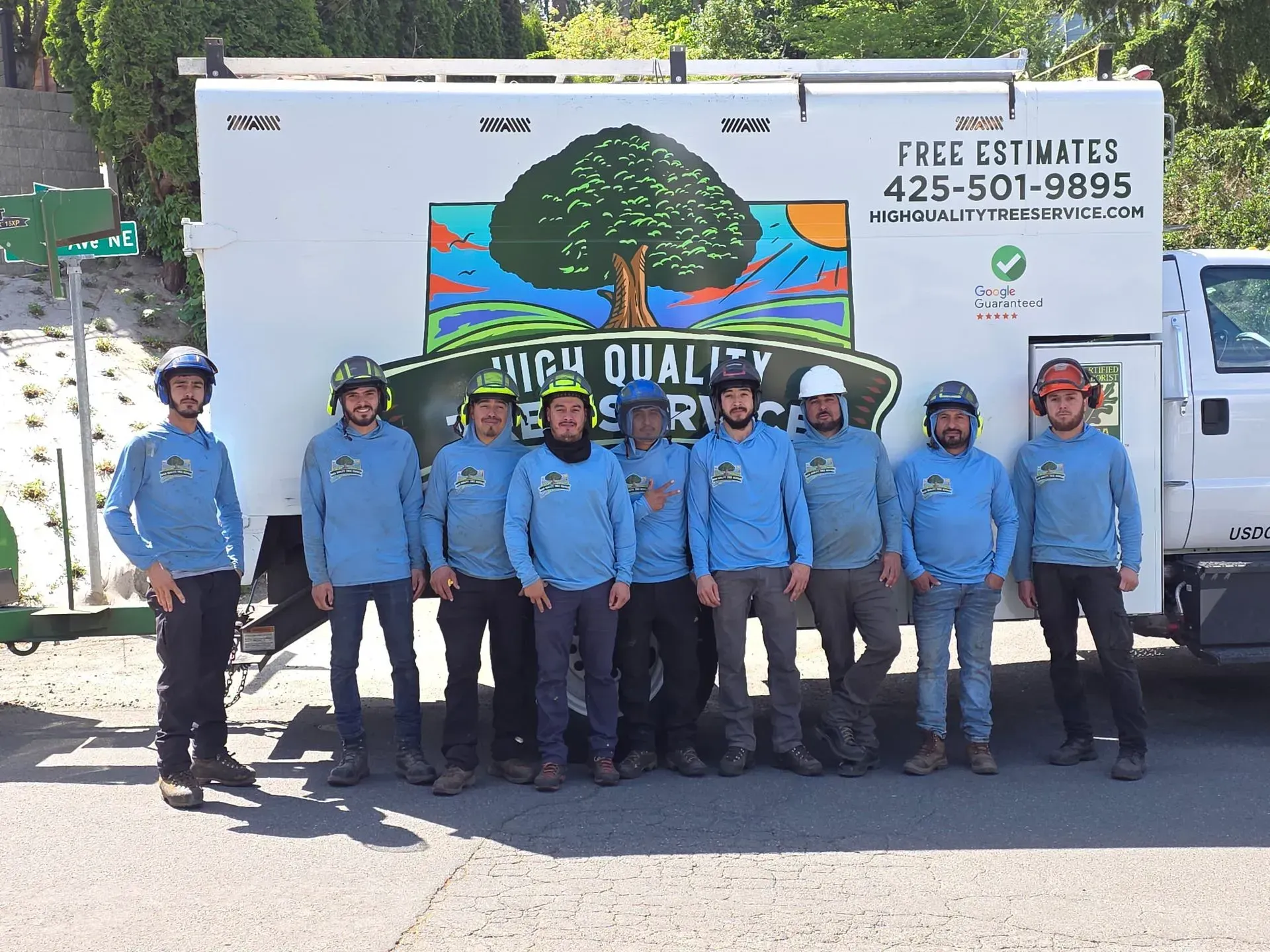 Group of workers in blue shirts posing in front of a food truck with a colorful tree mural.