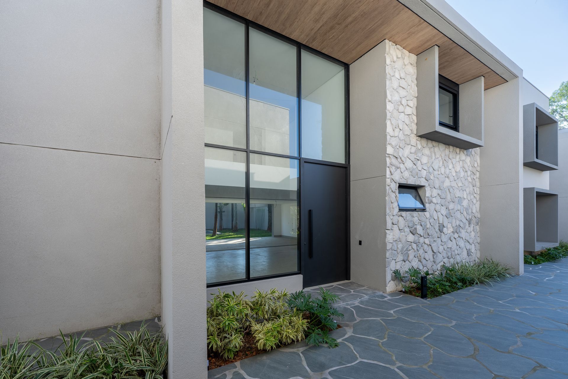 Uma casa moderna com uma grande porta de vidro e uma parede de pedra.