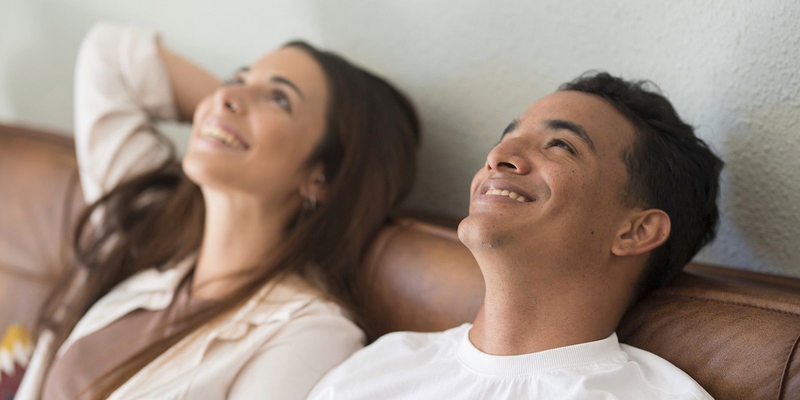 Two people smiling while looking up, reclining on a brown couch.