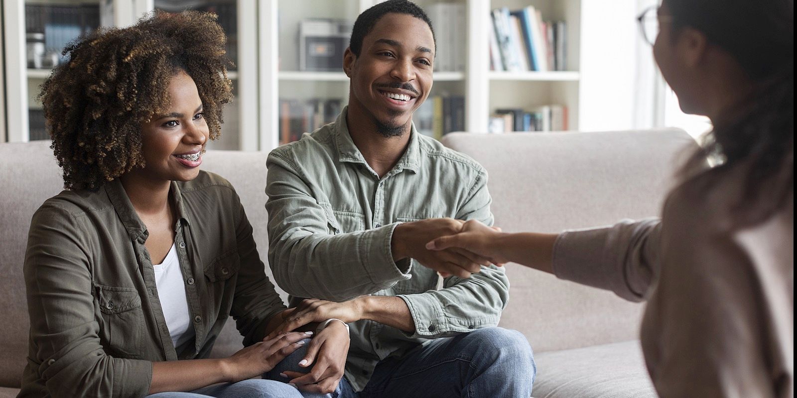 Couple shaking hands with a person, possibly a therapist. They are seated on a couch indoors.