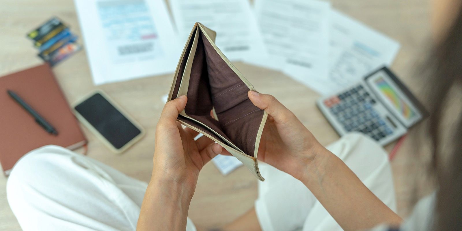 Person holding an empty wallet, surrounded by bills, a phone, and a calculator, illustrating financial problems.