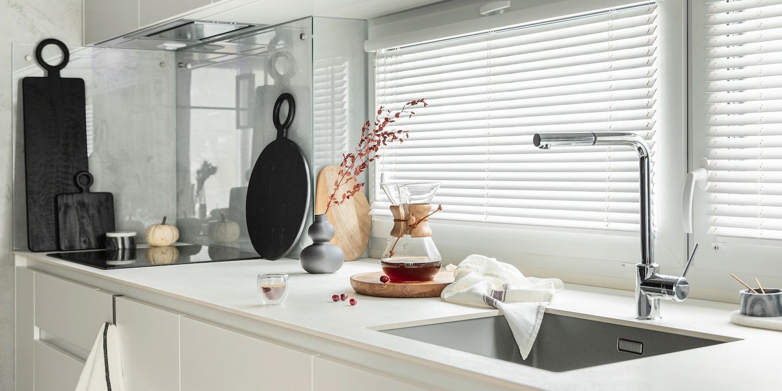 Kitchen with white countertops, sink, and window. Decorative cutting boards, vase with flowers, and a tea set.