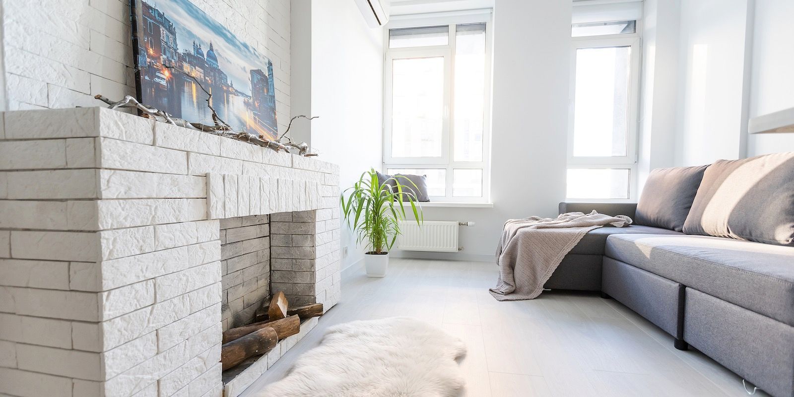 Living room with white brick fireplace, gray sofa, and large window.