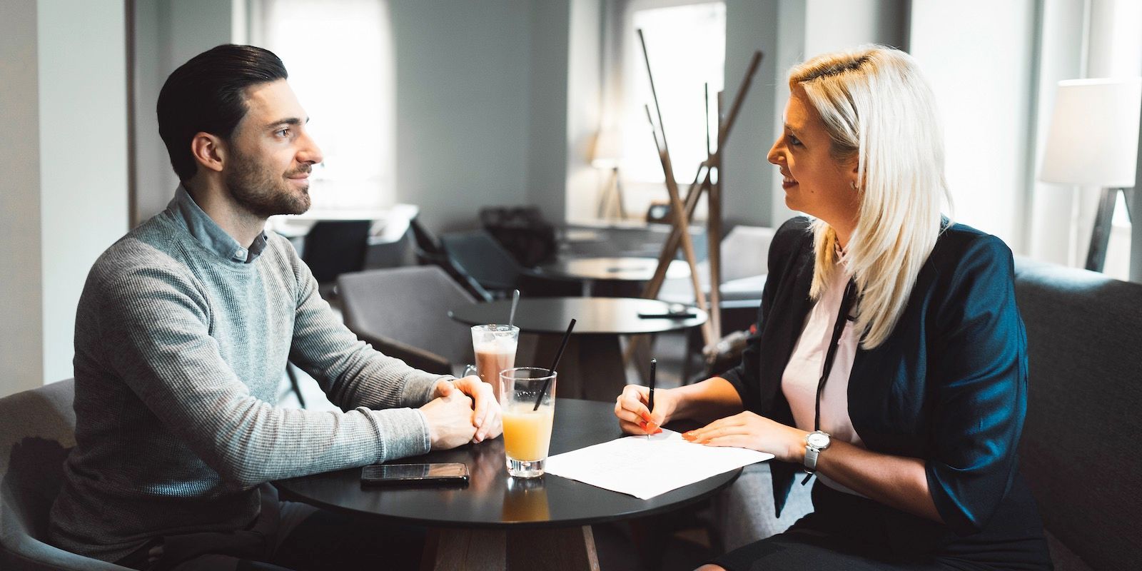 A man and a woman sit at a table, discussing documents. Drinks sit on the table as well.