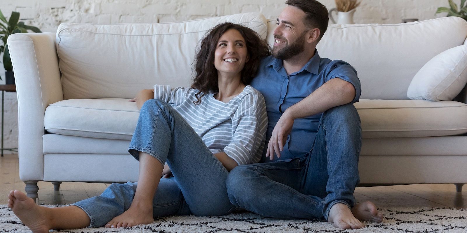 Couple sitting on the floor in front of a white couch, smiling.