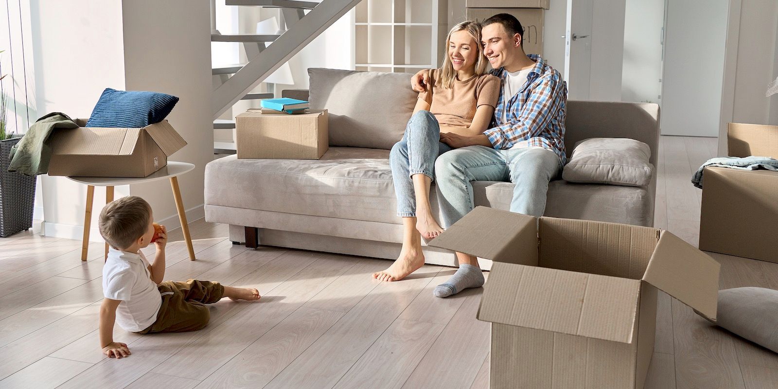 A family in a new home; a couple sits on a couch while their child sits on the floor. Boxes are visible.