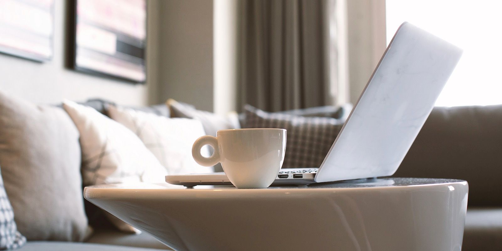 Laptop and coffee cup on a white table in front of a couch.