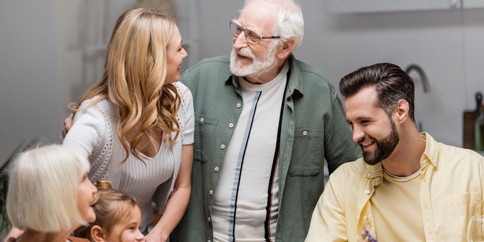 Family gathered together, smiling.  One woman has arm around another.  An older man smiles with another man.