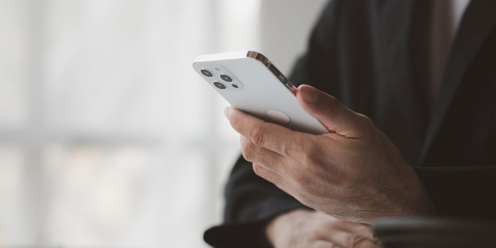 Close-up of a person holding a white smartphone, wearing a dark suit.