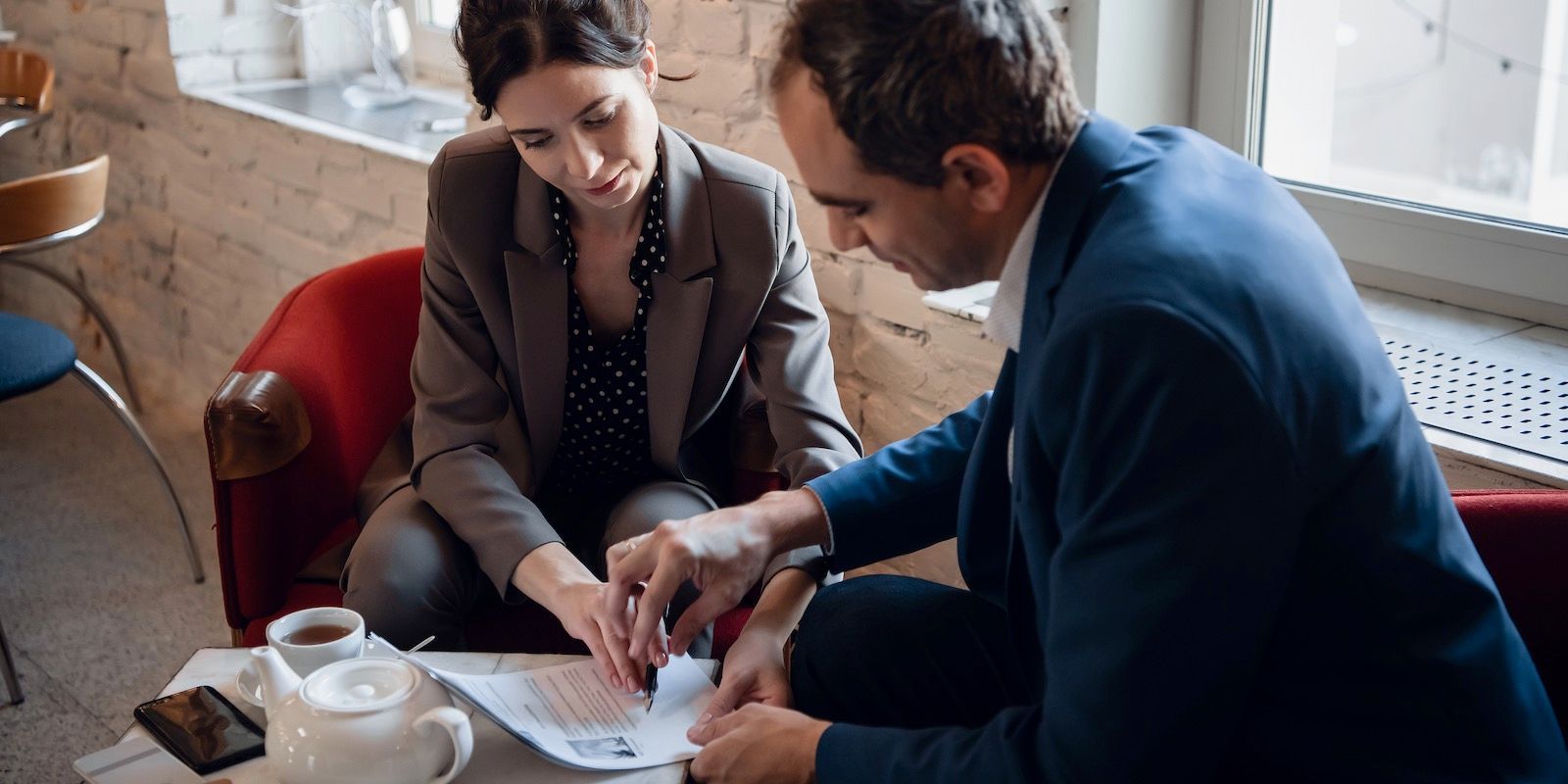 Two people in business attire examine documents at a table, possibly discussing details.