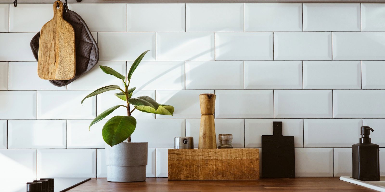 Kitchen counter with plant, cutting boards, pepper grinder, and soap dispenser against white tile.