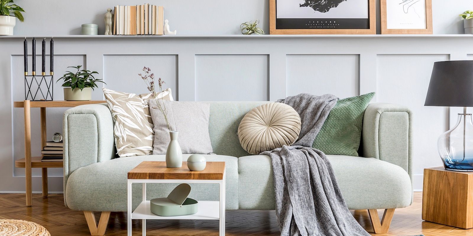 Living room with a light green sofa, throw pillows, blanket, side table, and wall shelf.