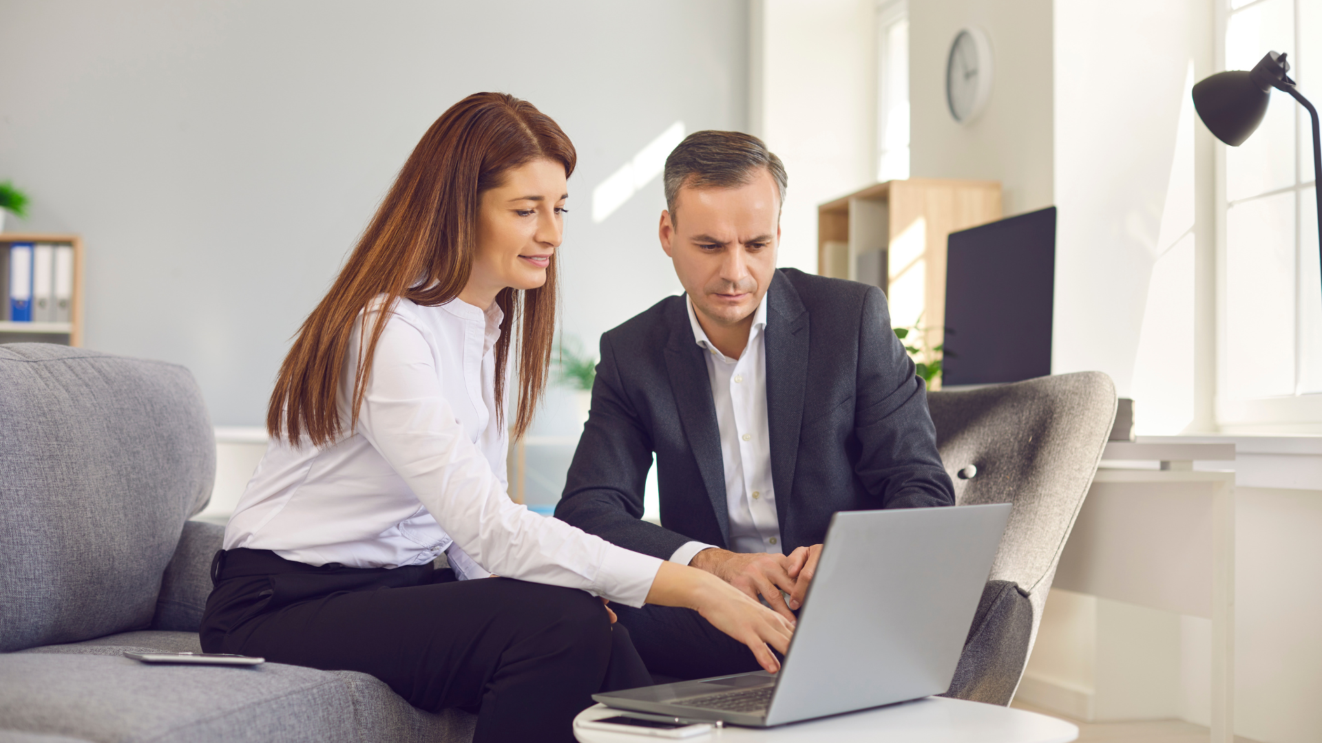 Woman pointing at laptop screen, collaborating with a man in an office setting.