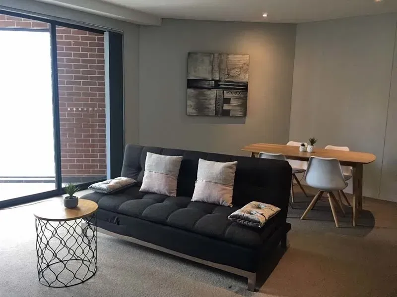 Modern living room with gray sofa, small round table, dining table, and artwork.