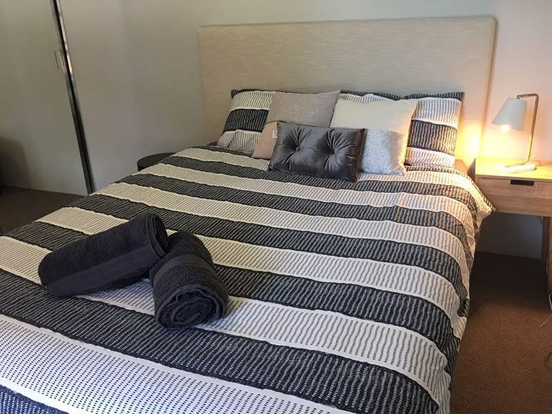 Bedroom with a striped comforter, pillows, towels, and a lamp on a nightstand.