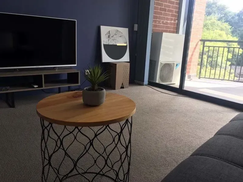 Living room with blue wall, TV, round coffee table, and balcony view.