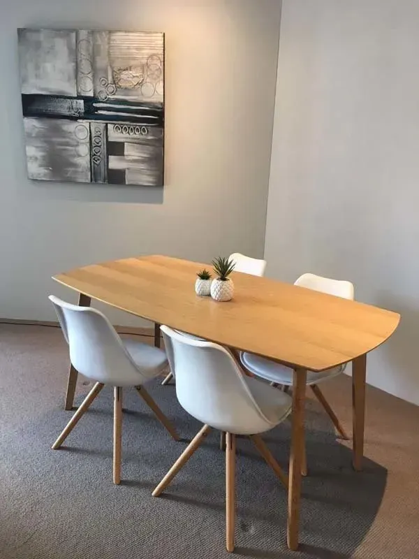 Dining table with four white chairs and small plants; abstract art on the wall.