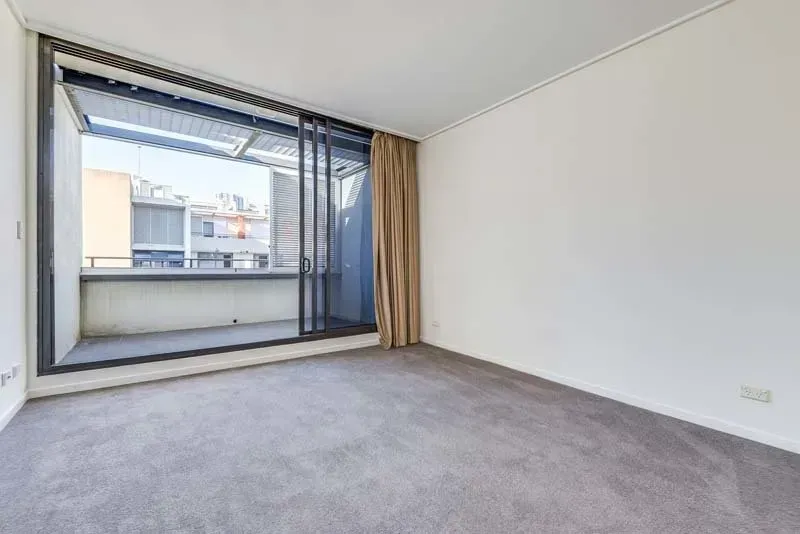 Empty room with gray carpet, large window, and beige curtains.