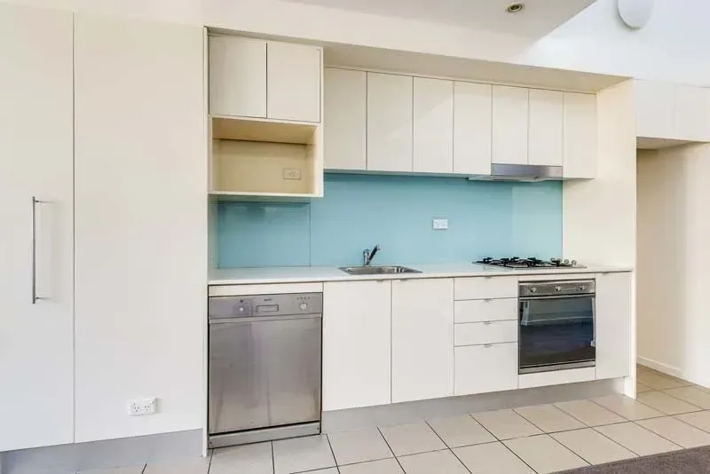 Modern kitchen with light cabinets, stainless steel appliances, and blue backsplash.