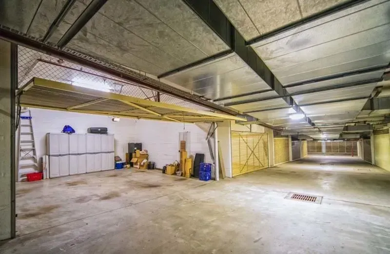 Empty concrete storage unit with a raised overhead door, stacks of boxes, and a metal ceiling.