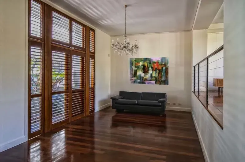 Living room with dark wood shutters, sofa, and painting; hardwood floor.