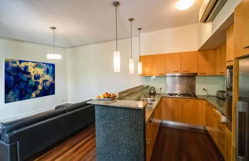 Modern kitchen with wooden cabinets, granite countertops, and a seating area with blue artwork.