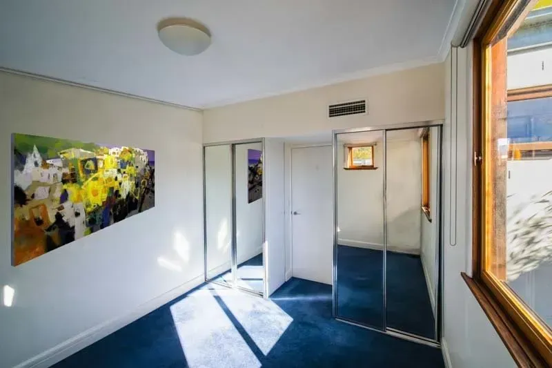 Hallway with blue carpet, white walls, and artwork, with large windows and mirrored doors.