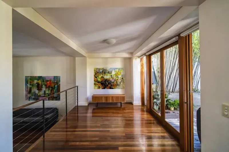Hallway with hardwood floors, art, a bench, and glass doors leading to a bamboo garden.