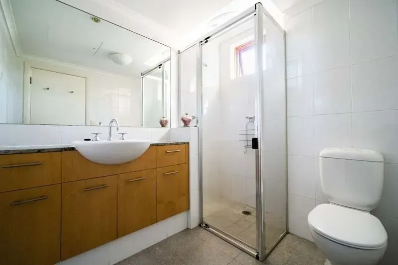 Bathroom with a white toilet, glass shower, brown vanity, and large mirror.