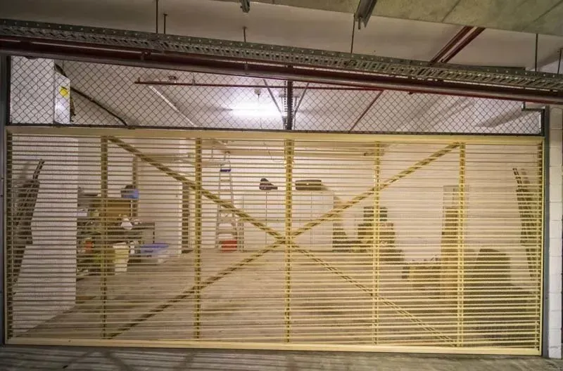 Yellow security gate inside a warehouse, with metal grid at the top and shelving visible.