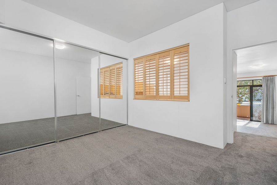 Empty bedroom with mirrored closet doors, carpet, and wooden shutters on a window.