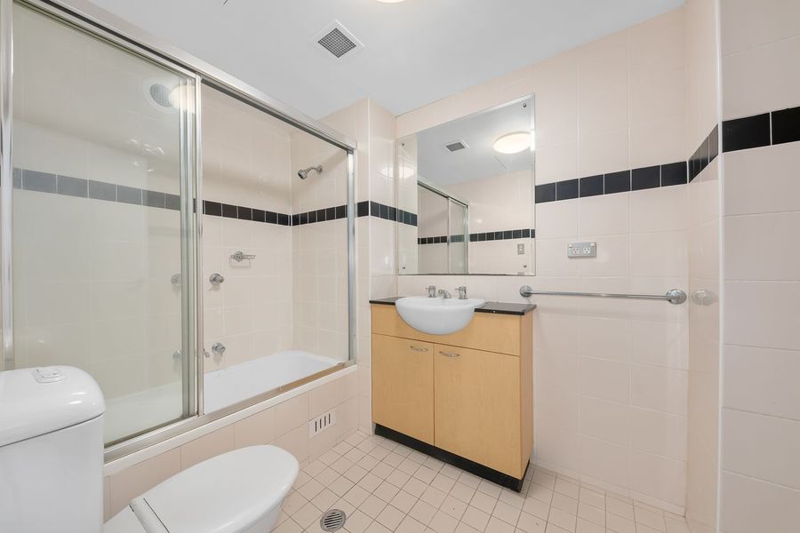 Bathroom with tub/shower, toilet, vanity, and mirror, white walls with black trim, beige floor tiles.