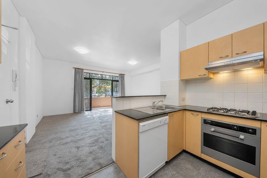 Kitchen with light wood cabinets, appliances, and a view into the living area with balcony.