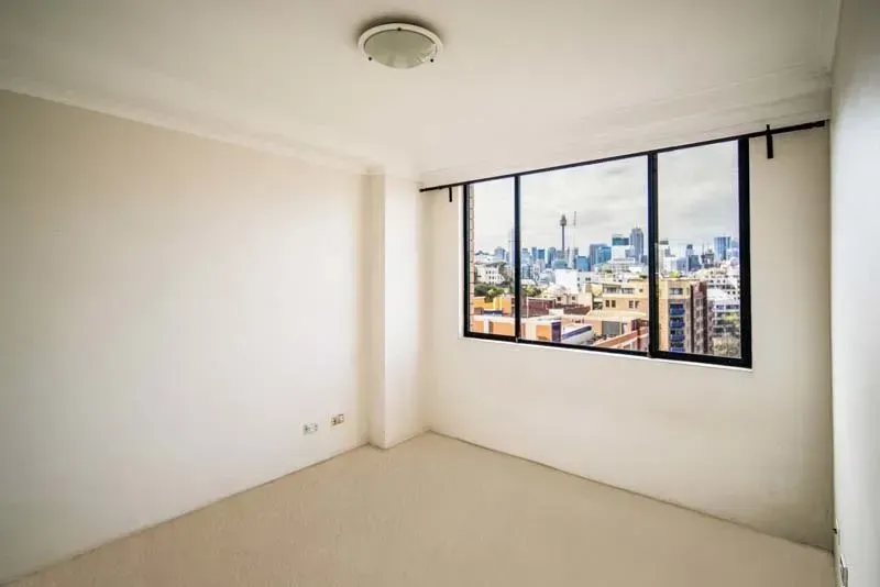 Empty, beige-walled room with a large window offering a city view.