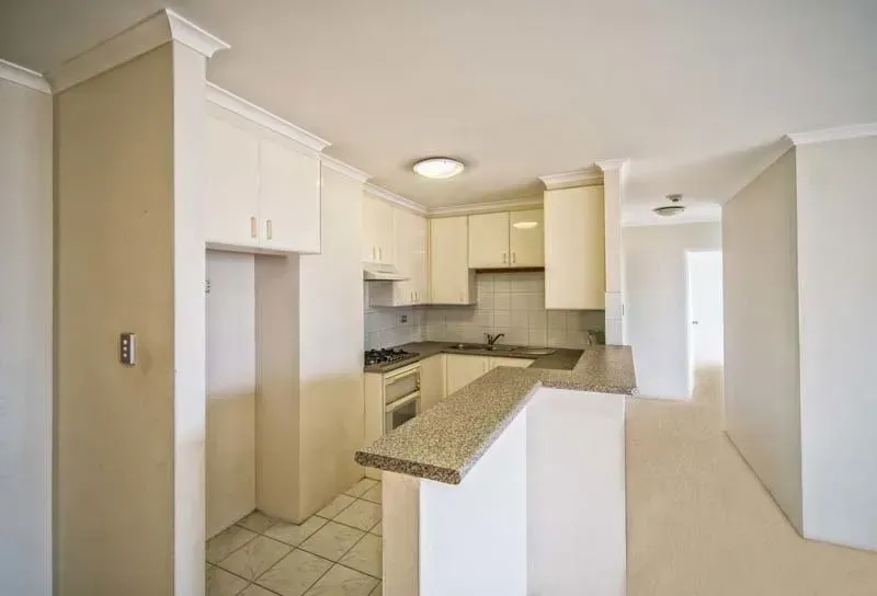Small kitchen with beige cabinets and granite countertops. Entryway with white walls and off-white carpet.