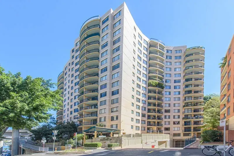 Tall beige apartment building with balconies, blue sky overhead.