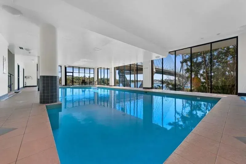 Indoor swimming pool with large windows offering a view, light blue water, beige tile surround.